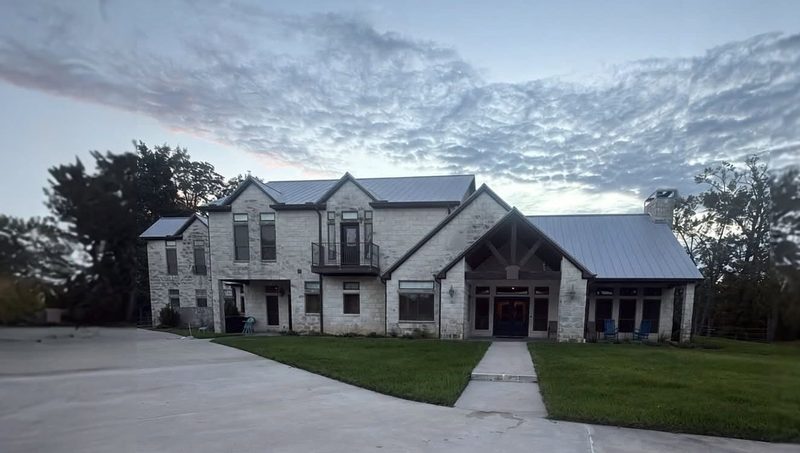 Two-story stone home with a standing seam metal roof by Built by Revitalize, photographed at dusk